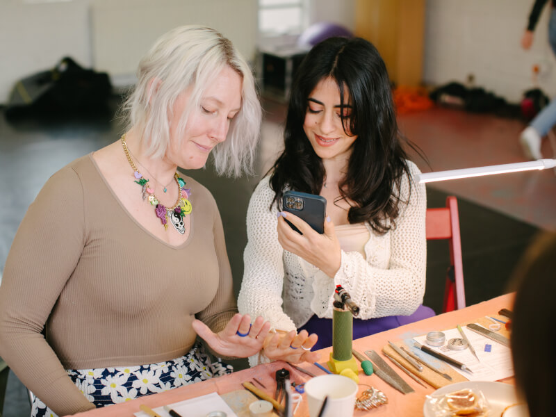 Two women smiling taking photo of their handmade rings